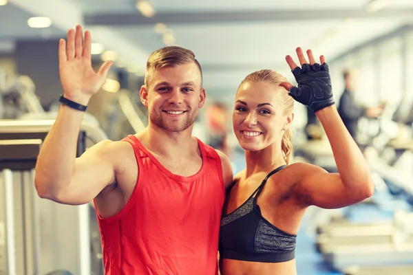 Sorridente homem e mulher acenando as mãos no ginásio — Fotografia de Stock