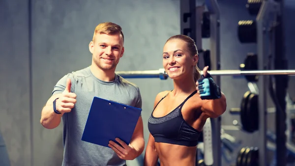 Glimlachende jonge vrouw met personal trainer in de sportschool — Stockfoto