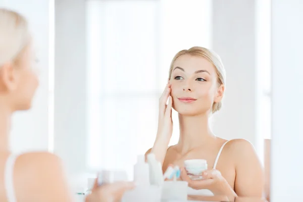 Glückliche Frau cremt Gesicht im Badezimmer ein — Stockfoto