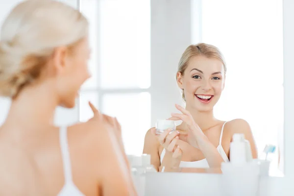 Mulher feliz aplicando creme no rosto no banheiro — Fotografia de Stock