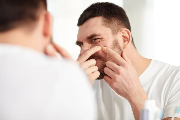 Man squeezing pimple at bathroom mirror — Stock Photo, Image