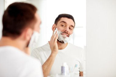 happy man applying shaving foam at bathroom mirror clipart