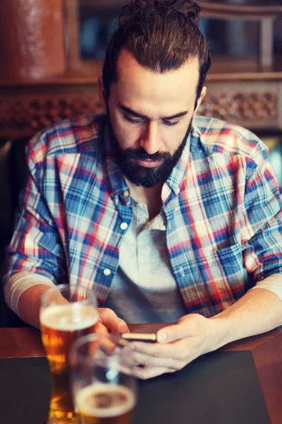 Человек со смартфоном пьет пиво в баре — стоковое фото