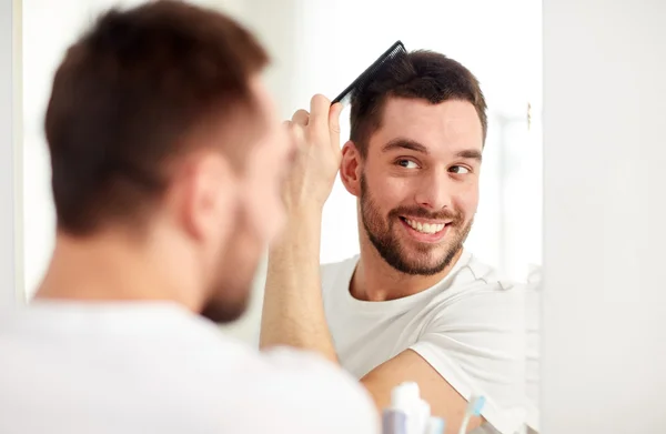 Happy man brushing hair  with comb at bathroom — Stock Photo, Image