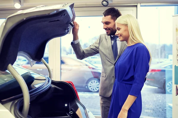 Casal feliz com revendedor de carro em auto show ou salão — Fotografia de Stock