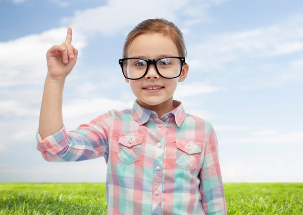 Lycklig liten flicka i glasögon pekar finger uppåt — Stockfoto