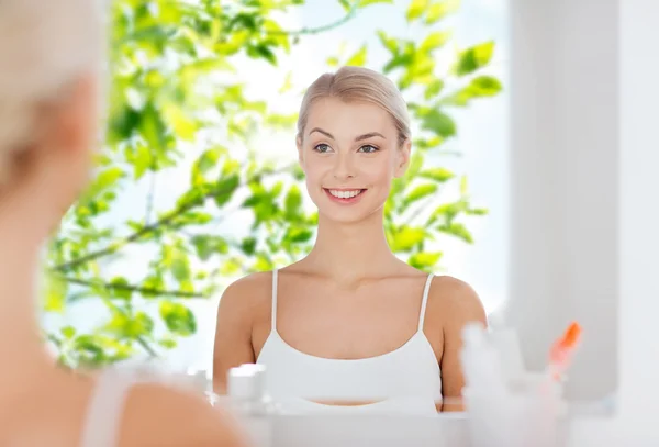 Happy young woman looking to mirror at bathroom — Stock Photo, Image