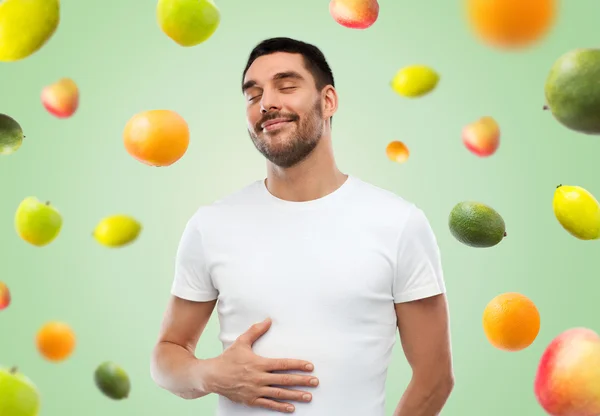 Happy full man touching tummy over falling fruits — Stock Photo, Image