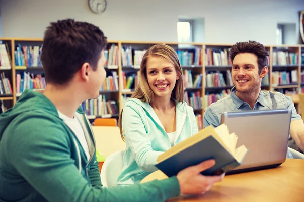 Estudiantes felices con portátil y libro en la biblioteca — Foto de Stock