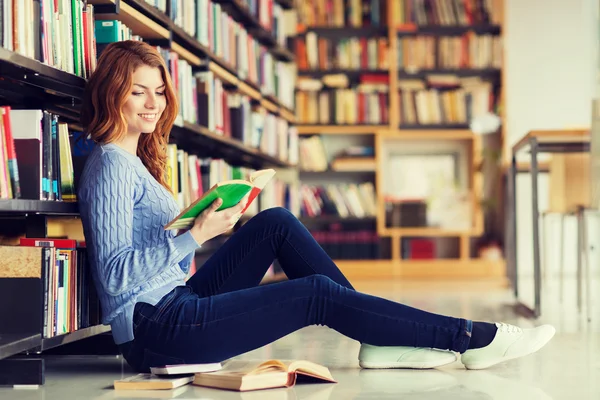 Счастливая студентка читает книгу в библиотеке — стоковое фото