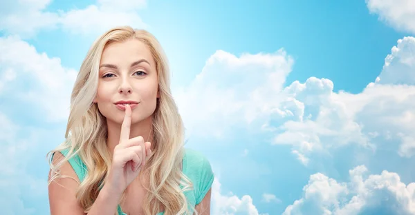 Beautiful young woman holding finger at her lips — Stock Photo, Image