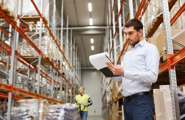 Businessman writing to clipboard at warehouse — Stock Photo, Image