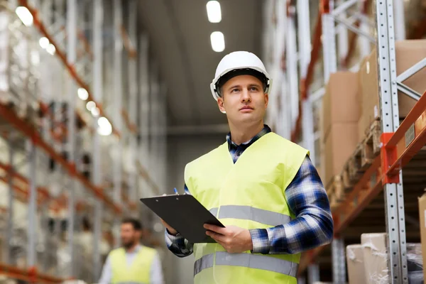 Man with clipboard in safety vest at warehouse — Stock Photo, Image