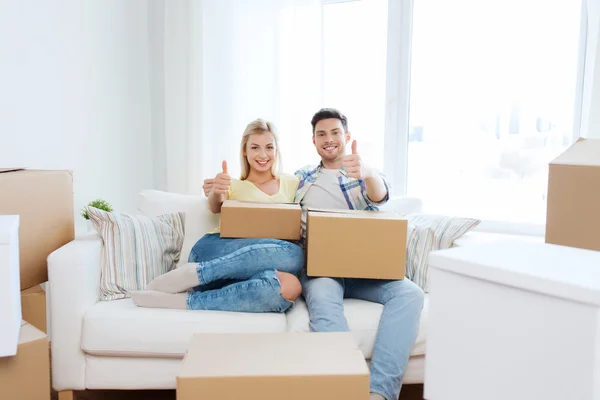 Feliz pareja con cajas mostrando los pulgares en casa — Foto de Stock