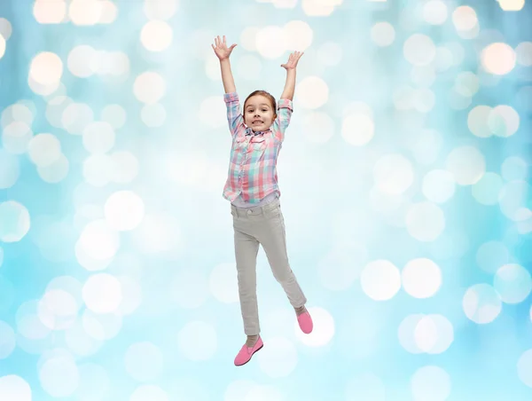 Happy little girl jumping in air over blue lights — Stock Photo, Image