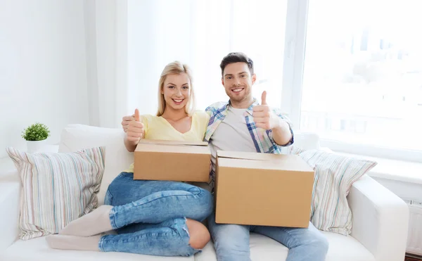 Casal feliz com caixas mostrando polegares para cima em casa — Fotografia de Stock