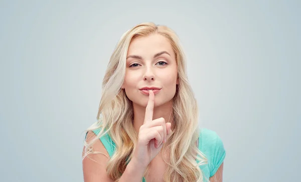 Beautiful young woman holding finger at her lips — Stock Photo, Image