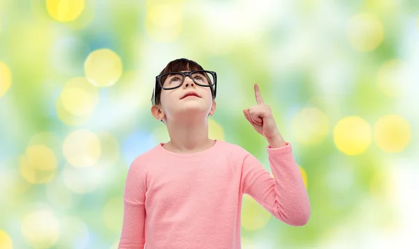 Happy little girl in eyeglasses pointing finger up — Stock Photo, Image