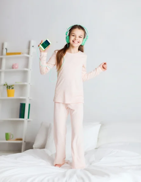 Chica saltando en la cama con teléfono inteligente y auriculares — Foto de Stock