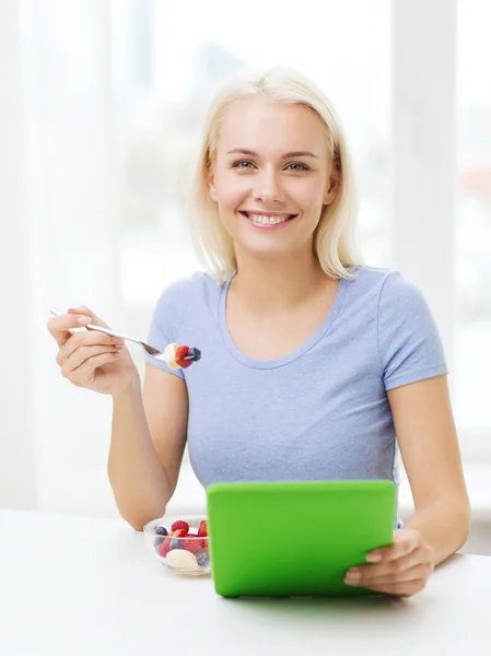Leende kvinna äta frukter med TabletPC hemma — Stockfoto