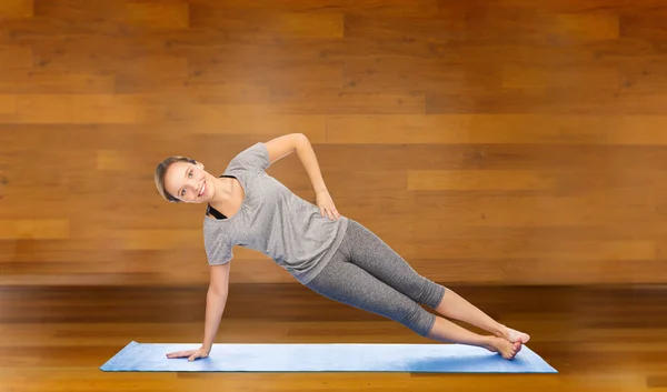 Mujer haciendo yoga en la postura lateral de la tabla en la estera —  Fotos de Stock