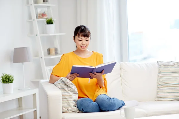 Sorridente giovane donna asiatica lettura libro a casa — Foto Stock