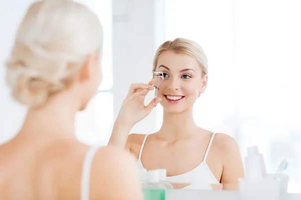 Woman with curler curling eyelashes at bathroom — Stock Photo, Image