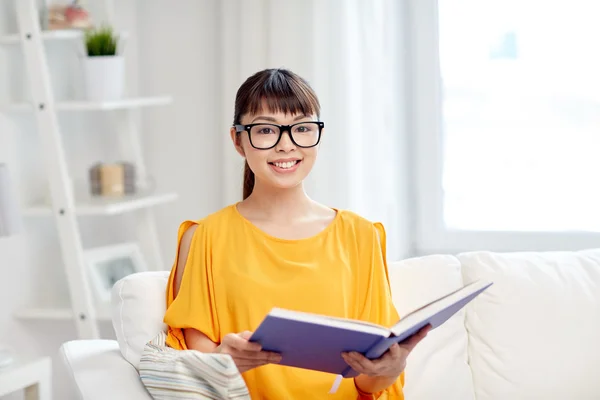 Smiling young asian woman reading book at home — Stock Photo, Image