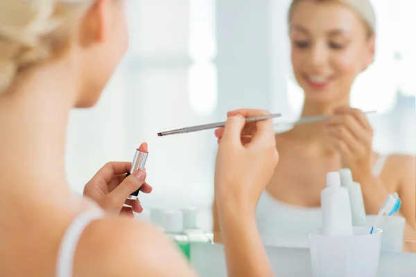 Femme avec rouge à lèvres et brosse à maquillage à la salle de bain — Photo