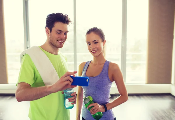 Mujer feliz y entrenador mostrando teléfono inteligente en el gimnasio — Foto de Stock