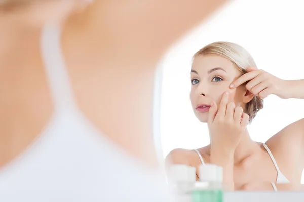 Woman squeezing pimple at bathroom mirror — Stock Photo, Image