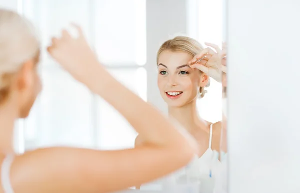 Woman with tweezers tweezing eyebrow at bathroom — Stock Photo, Image