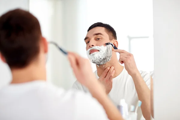 Мужчина бреет бороду. Мужчина бреет лицо. Мужское бритье. Мужчина с бритвой в ванной комнате.