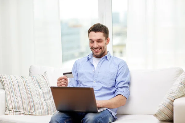 Uomo sorridente con computer portatile e carta di credito a casa — Foto Stock