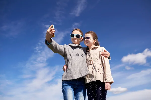 Счастливые девушки со смартфоном делают селфи на открытом воздухе — стоковое фото