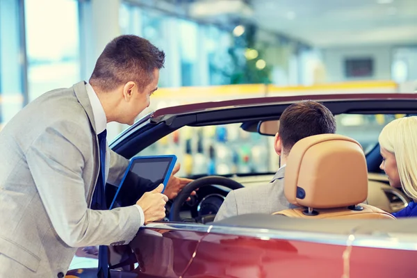 Casal feliz com revendedor de carro em auto show ou salão — Fotografia de Stock