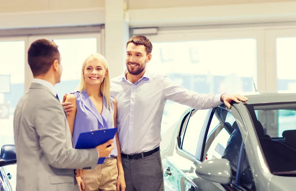 Casal feliz com revendedor de carro em auto show ou salão — Fotografia de Stock