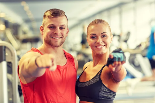 Happy man and woman pointing finger to you in gym — Stock Photo, Image