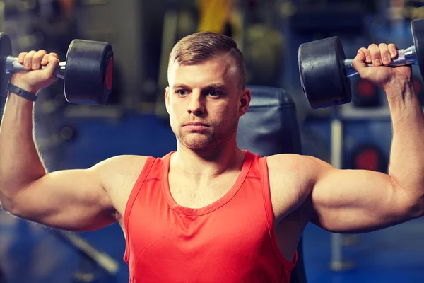 Young man with dumbbells flexing muscles in gym — Stock Photo, Image