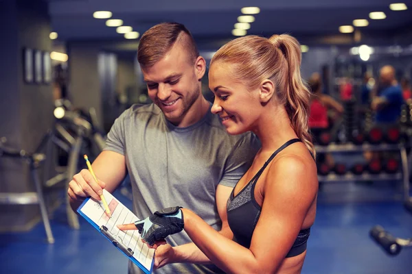 Lächelnde Frau mit Trainer und Klemmbrett im Fitnessstudio — Stockfoto