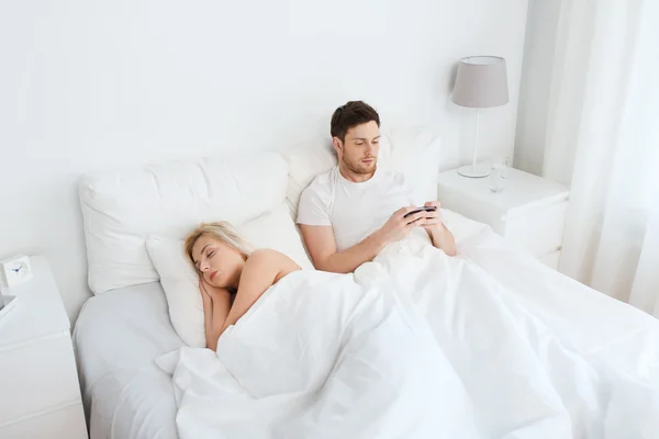 Man skicka SMS meddelande medan kvinnan sover i sängen — Stockfoto