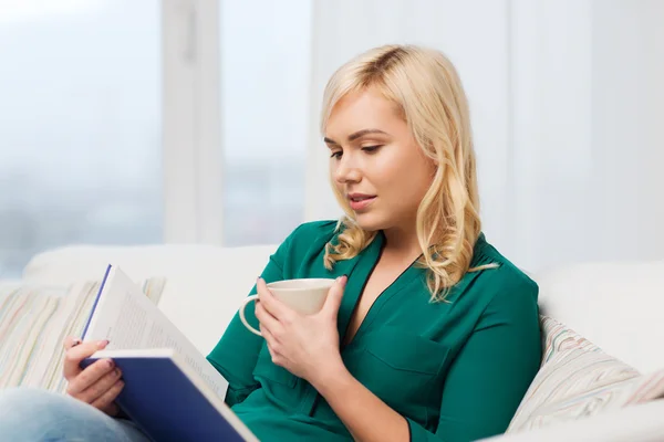 Jovem mulher com copo de chá livro de leitura em casa — Fotografia de Stock