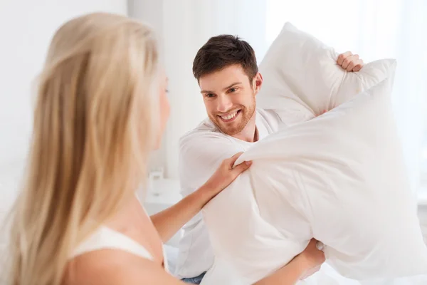 Šťastný pár s polštář bojovat v posteli doma — Stock fotografie