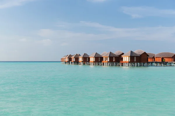 Bungalow huts in sea water on exotic resort beach — Stock Photo, Image