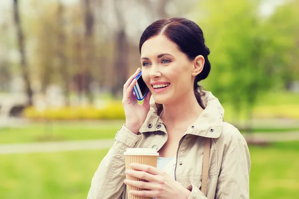 Lachende vrouw met smartphone en koffie in park — Stockfoto