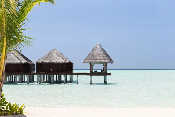 Bungalow huts in sea water on exotic resort beach — Stock Photo, Image