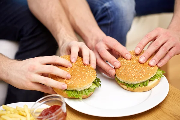 Close up de mãos masculinas com hambúrgueres na mesa — Fotografia de Stock