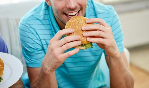 Close up of happy man eating hamburger at home — 스톡 사진