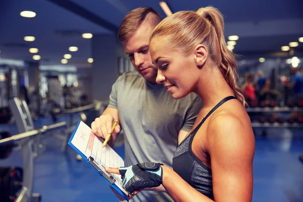 Lächelnde Frau mit Trainer und Klemmbrett im Fitnessstudio — Stockfoto