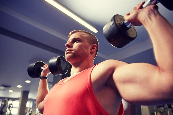 Young man with dumbbells flexing muscles in gym — Stock Photo, Image